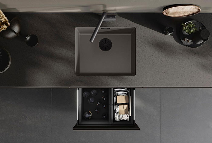Mørkt køkken set oppefra, med en komposit køkkenvask i vulkangrå, køkkenarmatur i samme farve og affaldssystem under vasken.